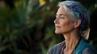 Serene mature woman with colorful hair enjoying peaceful moment in nature with eyes closed, radiating calm and mindfulness.