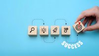 Business strategy concept with wooden blocks showing search, idea, rocket, teamwork and target icons leading to success on blue background.