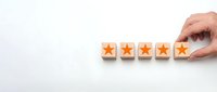 Hand placing wooden blocks with orange stars showing five star rating system for customer feedback and quality assessment on white background.