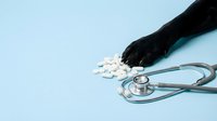 Close-up of gloved hand scattering white pills near stethoscope on light blue background, representing healthcare, medicine, pharmaceuticals, and medical practice for clinical or educational use.