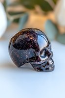 Dark crystal skull with deep purple and black inclusions on light background, showcasing mystical gemstone carving with detailed anatomical features.