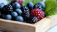 Fresh mixed berries including blueberries, blackberries and raspberries arranged in wooden serving tray with green leaf garnish, macro food photography.