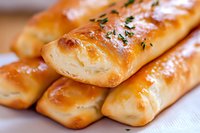 Fresh baked breadsticks with golden brown crust, sprinkled with herbs, arranged in rows on white linen. Close up macro shot showing flaky texture and buttery shine.