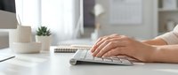 Female hands typing on white wireless keyboard at modern office desk with laptop and succulent plant in bright workspace for productivity and business.