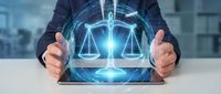 Businessman hands protecting glowing digital justice scales hologram on desk. Legal technology concept for law firms, attorneys, and judicial system innovation.
