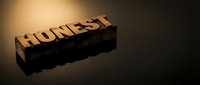 Wooden letter blocks spelling HONEST on dark surface with dramatic lighting and shadow reflection for business ethics and integrity concepts.