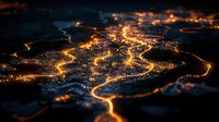 Aerial night view of glowing city streets forming an intricate network of golden light trails against dark landscape, captured with tilt-shift effect creating miniature appearance.
