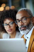 African American business colleagues in glasses looking at laptop screen during work meeting, showing professional collaboration and mentorship.