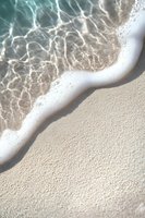 Gentle ocean wave washing up on pristine white sand beach with crystal clear turquoise water creating natural patterns and ripples in sunlight.