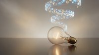 Modern lightbulb with glowing digital icons spiral above representing innovation, technology and creative ideas for business solutions and smart concepts.