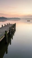 Wooden pier extending into calm lake at sunrise with moored boat and misty forested shoreline, suitable for travel, nature, and wellness marketing materials.