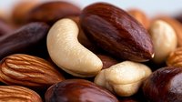 Mixed raw nuts including cashews, almonds and macadamia in macro close up view showing natural texture and patterns of healthy protein rich snacks.