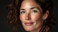 Portrait of middle-aged Caucasian woman with natural freckles and curly brown hair against dark background, showcasing authentic beauty and confidence.