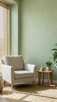 Serene living room corner with beige armchair, wooden side table, potted plants, and natural light from woven window shade against soft green wall.