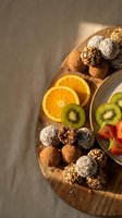 Assorted chocolate energy balls with coconut and nuts served on wooden board with fresh orange and kiwi slices for healthy snacking and dessert presentation.