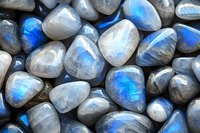 Polished moonstone and labradorite crystals displaying vibrant blue flash and iridescence, arranged in natural pattern for spiritual and healing practices.