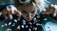 Young blonde woman experiencing mental health crisis with scattered medication pills around her face showing distress and psychological struggle.