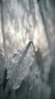 Macro close-up of frost crystals forming on dark wood surface with shallow depth of field, creating abstract winter texture and seasonal nature details.