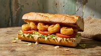 Crispy fried shrimp po boy sandwich with lettuce and tomato on crusty bread, served on rustic wooden table for restaurant menu and food advertising.