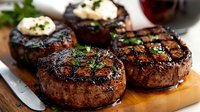 Juicy grilled beef tenderloin steaks topped with herb butter and fresh parsley on wooden cutting board, close-up view showing charred grill marks and medium rare doneness.