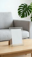 Empty glass picture frame on wooden table in modern living room with gray sofa and monstera plant for home decor and interior design mockup.