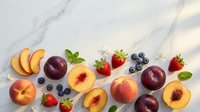 Fresh summer fruits including peaches, plums, strawberries and blueberries arranged on elegant marble surface for healthy eating and cooking concepts.