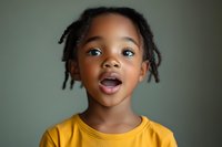 Young African American child with surprised excited expression wearing yellow t-shirt against blurred background, displaying genuine emotion and joy in candid portrait.