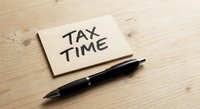 Sticky note with tax time reminder and black pen on wooden desk surface for financial planning and accounting preparation deadline concept.
