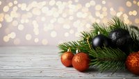 Festive Christmas decoration with black and orange ornaments on pine branches against bokeh lights on wooden surface. Perfect for holiday designs.