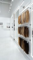 Modern hair extension salon interior with organized blonde brown hair pieces displayed on wall mounted racks in clean white minimalist beauty studio space.