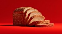 Freshly sliced whole grain bread loaf on vibrant red background, showcasing texture and layers for food photography and culinary marketing.