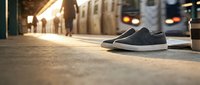 Black canvas sneakers on urban subway platform with commuter train and warm sunlight creating atmospheric transit scene for lifestyle advertising.