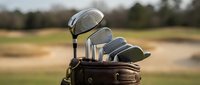 Golf clubs in leather bag on course with blurred fairway background. Professional equipment for sport and recreation activities on sunny day.