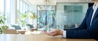 Professional in dark suit holding glowing digital globe hologram at wooden desk in modern office with plants and windows, representing global business, technology, and international commerce.