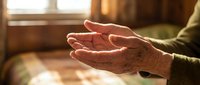 Elderly hands cupped in prayer or meditation gesture with warm sunlight streaming through window creating peaceful spiritual moment for wellness concepts.