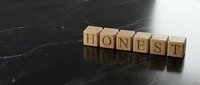 Wooden letter blocks spelling HONEST on dark marble surface representing integrity, trust, ethics and moral values in business and personal relationships.
