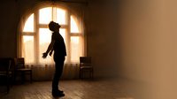 Young man silhouette standing in sunlit room with arched window, dramatic lighting creates contemplative atmosphere for wellness and mindfulness concepts.