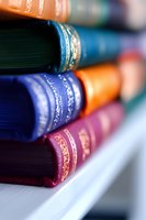 Stack of colorful vintage books with gold embossed spines on white shelf, macro close-up view showing rich leather textures and ornate binding details.