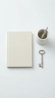 Minimalist flat lay composition with blank hardcover book, ceramic cup with spoon and vintage key on white background for creative projects.