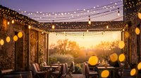 Outdoor patio with string lights and glowing lanterns at sunset, featuring comfortable seating and rustic brick walls for entertaining and relaxation.