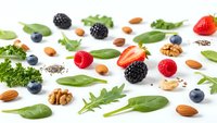 Fresh organic superfood ingredients scattered on white background including berries nuts leafy greens for healthy nutrition and wellness lifestyle.