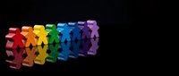 Colorful paper cutout figures holding hands in rainbow spectrum creating unity chain on black background for diversity and inclusion concepts.