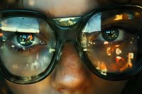 Close up view of eyes behind eyeglasses reflecting city lights and bokeh effect, creating dreamy atmospheric mood with warm evening glow and urban reflections.