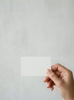 Caucasian hand holding blank white business card against neutral gray textured background, suitable for branding, corporate identity, and marketing mockup designs.