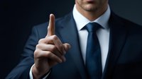 Businessman in navy suit raising index finger to make important point during corporate presentation against dark background.