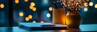 Cozy evening workspace with notebook, pencils and dried flowers against blurred bokeh lights background creating warm atmospheric home office setting.