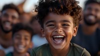 Young mixed-race boy with curly hair laughing joyfully, showing bright white teeth and genuine happiness, wearing casual green t-shirt against blurred group background.