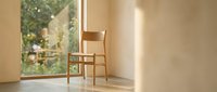 Wooden chair positioned by large window with natural sunlight streaming into minimalist interior space, suitable for home decor and interior design projects.
