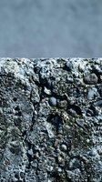Rough textured asphalt surface with embedded stones and pebbles against cloudy sky background for construction and road infrastructure projects.
