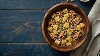 Homemade granola with nuts and dried fruit pieces in wooden bowl on rustic blue table for healthy breakfast and snacking.